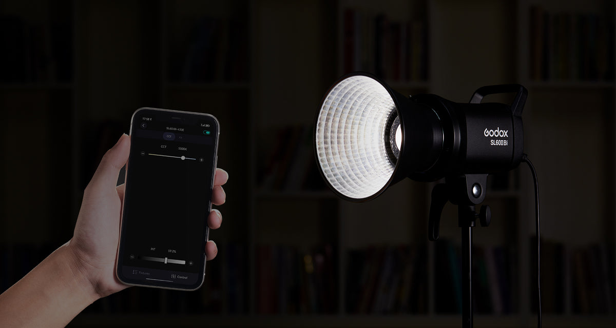 Hand holding a phone showing a control app beside a Godox SL60II-series light on a stand