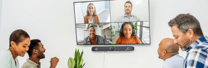 Poly Studio X52 video bar mounted below a wall display showing four remote participants during a video call