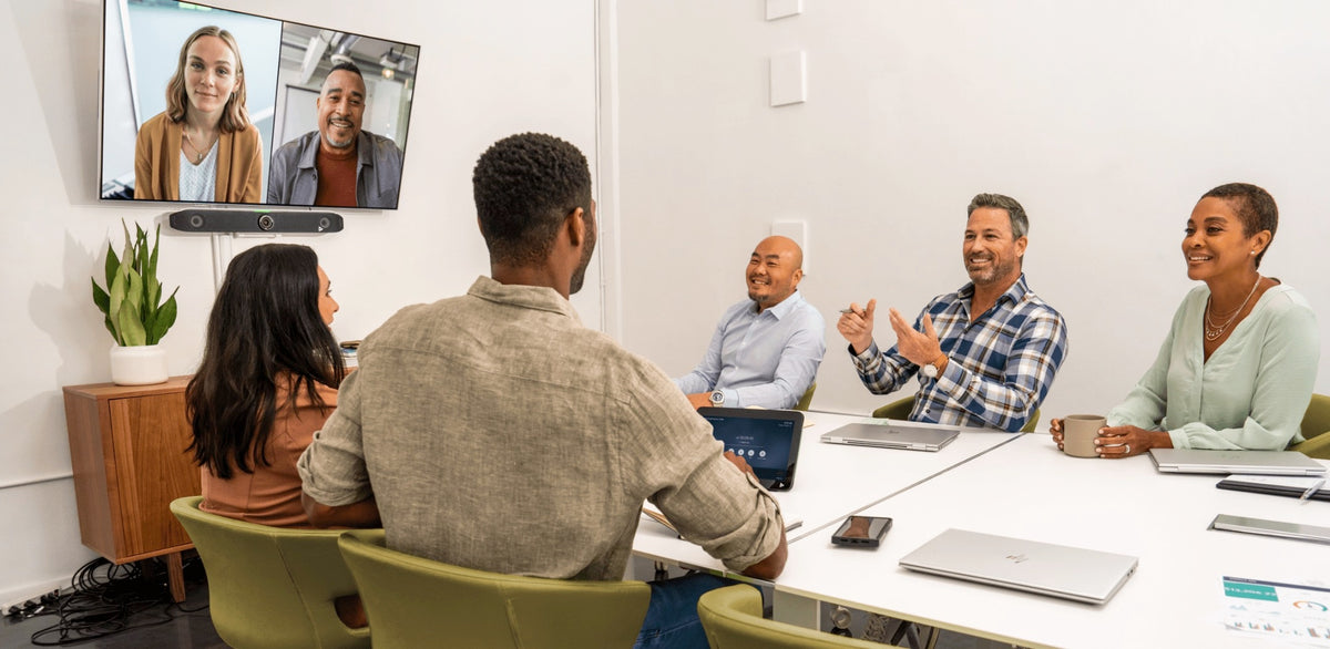 Poly Studio X52 video bar below a wall display in a medium meeting room, with remote participants on screen