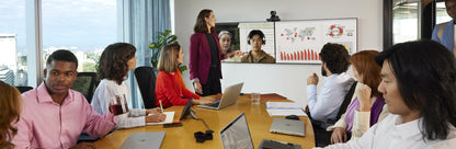 Hybrid meeting in a large conference room with colleagues at a table and a remote participant on the wall display