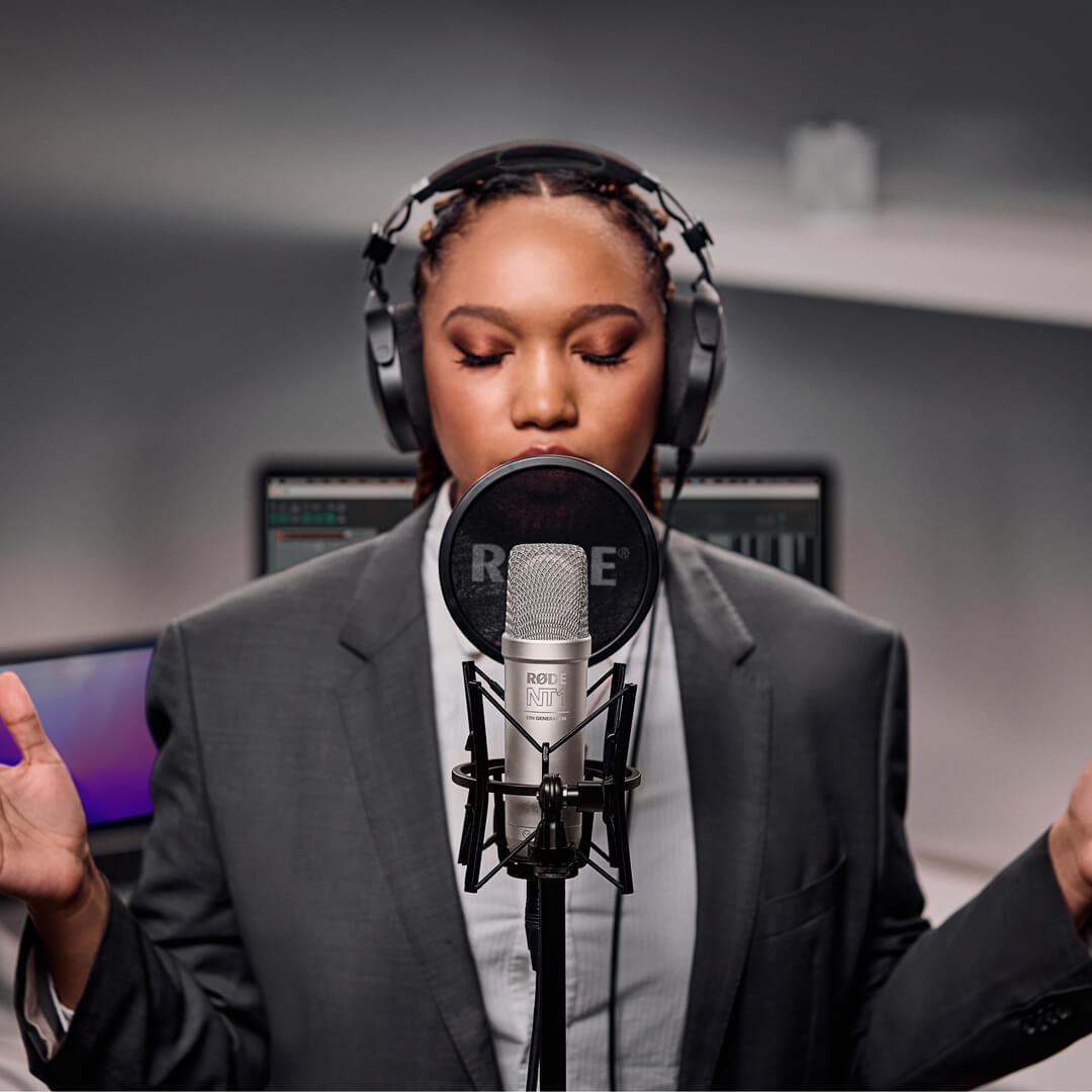 Singer wearing headphones recording with a silver RØDE NT1 5th Generation microphone and pop filter